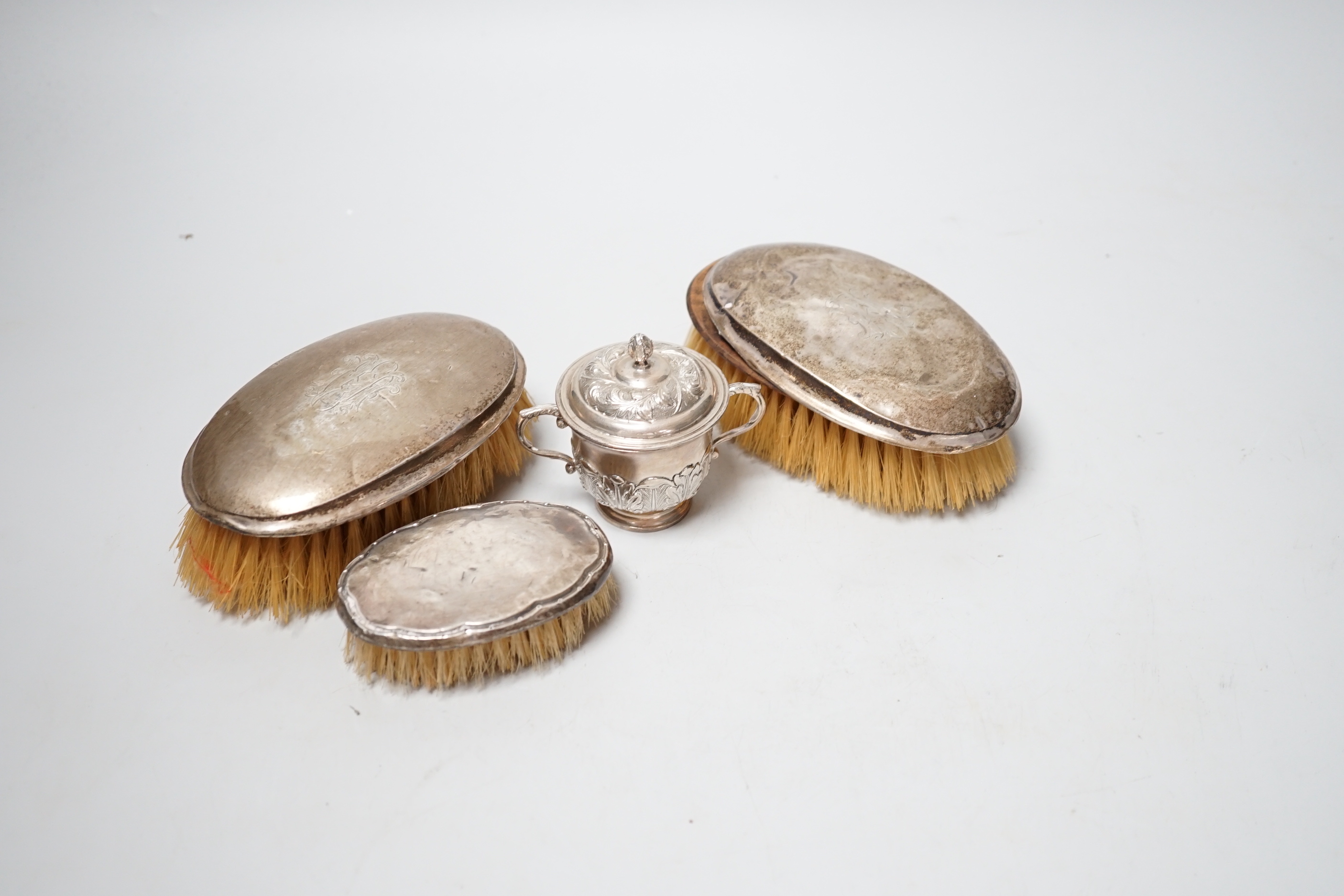 A small George V silver twin handled cup and cover, London, 1929 and three silver mounted brushes.